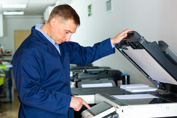 Portrait of confident service engineer standing by photocopy machine in office. High quality photo