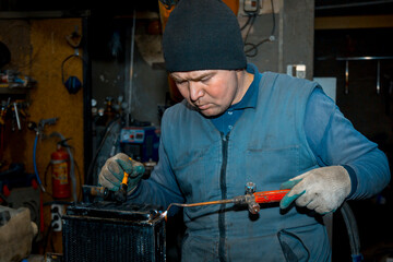 Welder cleans a copper car radiator with a metal brush and a torch