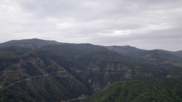 "golden hour" head-on drone video moving over the mountains of SH22 in albania, above the road on top of the hill. Cloudy sky and some small houses can be seen.