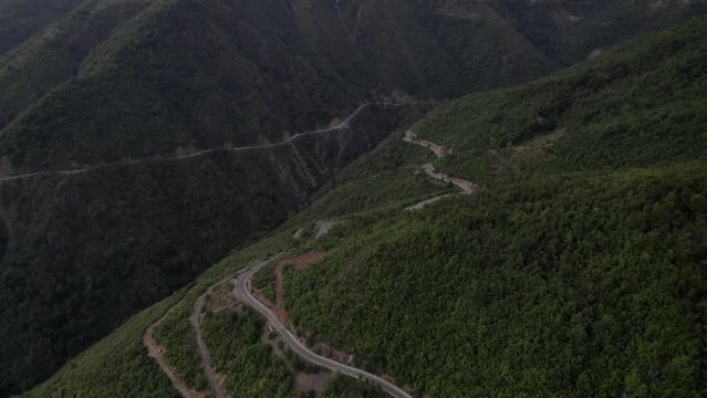 "golden hour" front descriptive panning drone video moving over the SH22 mountains in albania, above the road on top of the hill. Cloudy sky and some small houses can be seen.