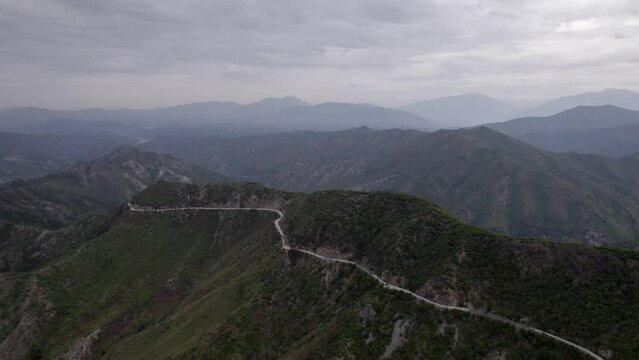 "golden hour" head-on drone video moving over the mountains of SH22 in albania, above the road on top of the hill. Cloudy sky and some small houses can be seen.