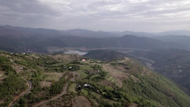 Front drone video in "golden hour" advancing over the mountains of SH22 in albania, over the village of Va Spas and in the background Lake Drin. the cloudy letting the sun's rays through.