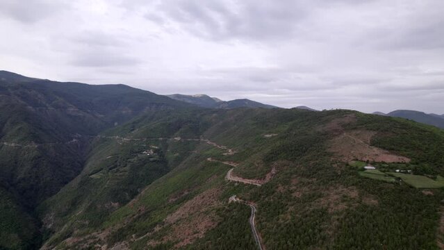 "golden hour" head-on drone video moving over the mountains of SH22 in albania, above the road on top of the hill. Cloudy sky and some small houses can be seen.