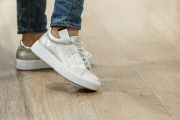 Woman tries on new casual silver leather sneakers with white sole.