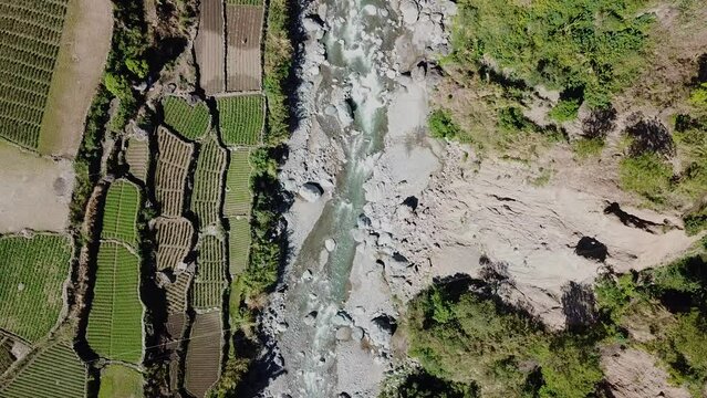 rocky mountain river water flowing next to farms rice paddy terrace gardens sunny day mountain community in remote area of Kabayan Benguet Philippines stationary wide angle bird's eye view