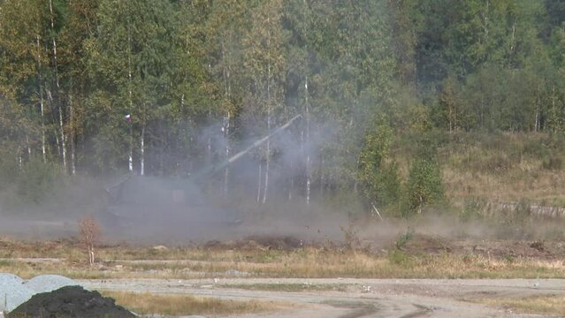 A tank covered with camouflage fabric fires a cannon at a target. Russian heavy weapons, exercises at the training ground.