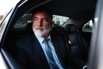 Mature handsome businessman is sitting in luxury car. Serious bearded man in suit.