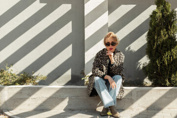 Stylish beautiful young blonde woman with sunglasses in a fashionable leopard coat with flared...