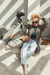 Two beautiful funny hipster women friends in fashionable clothes and shoes pose outside on a warm sunny spring day