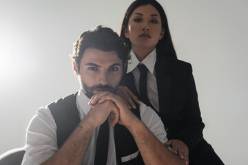 stylish interracial couple in formal wear looking at camera on grey background