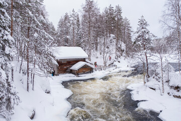 Winter landscape, a log house on the bank of a river with a rift. Oulanka National Park Kuusamo Finland, snowy forest.