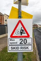 Temporary road sign attach to a lamppost warning of a skid risk and stipulating a speed limit.