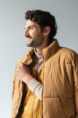 happy and stylish man in warm puffer jacket looking away isolated on grey