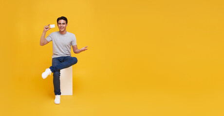 Fototapeta na wymiar Happy handsome Asian man showing credit card for making payment or paying online business in hand isolated on yellow background.