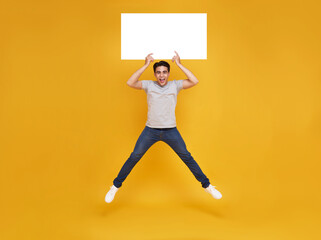 Smiling happy Asian man jumping and holding blank speech bubbles on yellow background. advertise announcement concept.