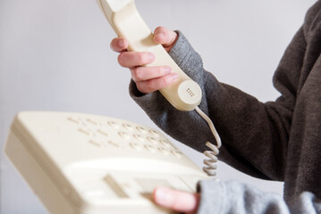 Detalle de una mano de mujer descolgando un teléfono blanco antiguo con cable. Mano sosteniendo el...