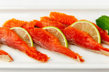 Pieces of red fish with lime on a white plate. Delicious and healthy snack. Close-up.