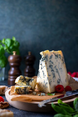 Blue cheese, dor blue or roquefort mold cheese slice on cutting board with basil leaves and...