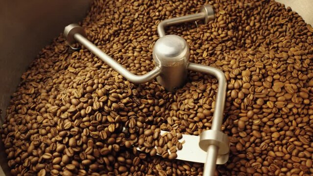 Production of freshly roasted coffee beans. Industrial mixing machine mixes roasted coffee beans in roaster, close up. Roasting process in factory. Food and drink background for cafe. Slow motion.