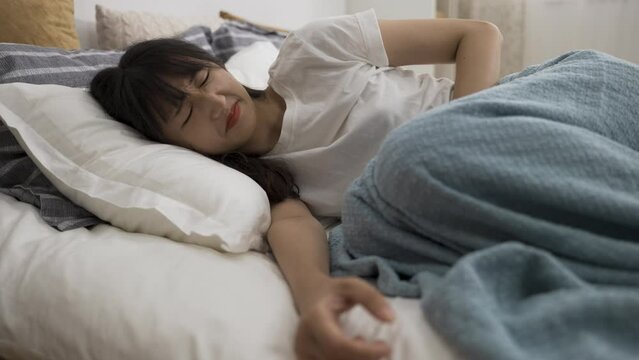 asian woman lying huddling up on bed and holding her belly while suffering menstrual pain in the bedroom at home.