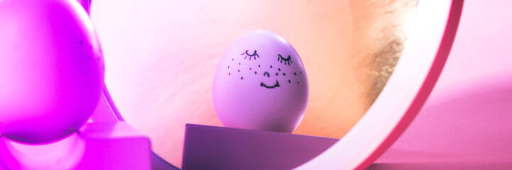 Easter holiday concept with cute handmade egg. Cute face egg looks in the mirror on a pink background with neon light. Banner