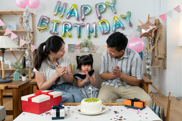 loving asian father and mother looking at their cute baby girl as they are singing happy birthday...