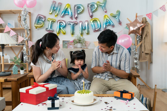 loving asian father and mother looking at their cute baby girl as they are singing happy birthday song and celebrating her two year old birthday at home