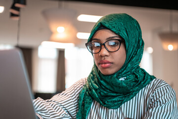 Business woman wearing a green hijab using laptop in relaxation area at modern open plan startup office. Selective focus 
