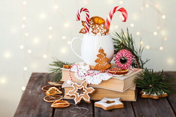 Fototapeta na wymiar Hot winter drink in a white mug: cozy home composition with homemade gingerbread cookies, candy cane, fir tree branch. Wooden background, christmas lights and candles