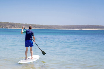 Man wearing rash guard on a stand-up paddle board at the ocean bay in Australia. SUP water sport activity