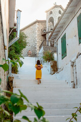 Fototapeta na wymiar Young traveller woman in yellow dress back view walking in old greece town.