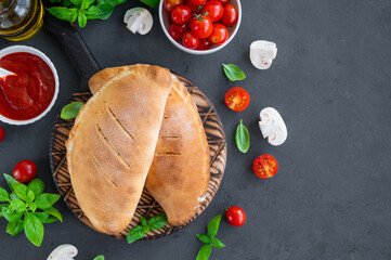 Traditional closed Italian calzone pizza with tomato sauce, mozzarella cheese and mushrooms on a board on a dark background. selective focus, top view, copy space.