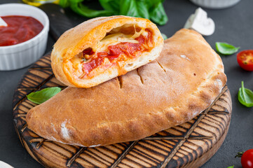 Traditional closed Italian calzone pizza with tomato sauce, mozzarella cheese and mushrooms on a board on a dark background. selective focus