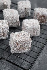 Traditional Australian Lamington cake in chocolate glaze and coconut flakes on a gray concrete background. Selective focus.