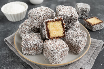 Traditional Australian Lamington cake in chocolate glaze and coconut flakes on a plate on a gray concrete background with a cup of tea. Selective focus.