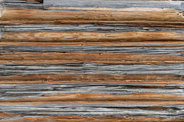 Texture of wooden wall of ancient barn made with weathered brown and grey planks and logs at bright sunlight in country house yard extreme close view