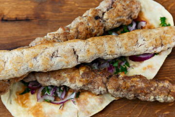 Appetizing barbecue on skewers with fresh vegetables on a flatbread. Top view. Close-up.