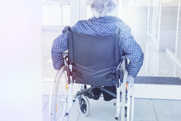 Elderly person with dependency and mobility problems due to bone disease sitting in a wheelchair. Close-up of wheel and hands in wheelchair while moving forward in solitude. Photo in a nursing home.