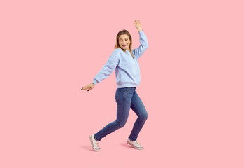 Female model having fun in the fashion studio. Cheerful young girl dancing and laughing. Full body shot of a pretty woman in comfortable casual outfit dancing isolated on pastel pink colour background