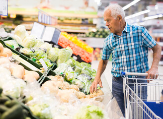 Mature senor examines turnip in the vegetables section of supermarket