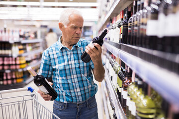 elderly retired senor buying wine in the alcohol section of the supermarket