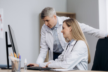 Two doctors talking at workplace looking at computer screen, analyzing results of patients medical examination, feeling satisfied with good news.
