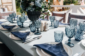 Blue glasses, plates and utensils on a festive table with flowers.