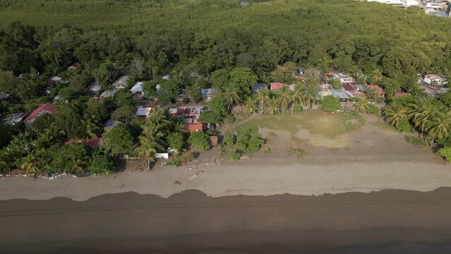 The tin hut village El Cocal bordering the pacific ocean near Quepos, Costa Rica on a sunny day. Aerial sideways tracking shot.