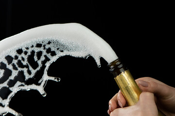 Female hand uncorks bottle of champagne on black studio background. Explosion of sparkling white...