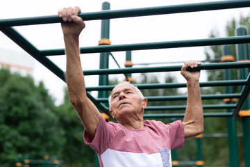 Obraz premium Active grandfather moves with the help of his hands on a horizontal ladder on sports ground