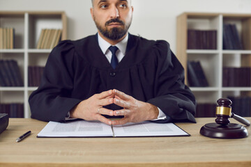 Judge sitting at his table in the courtroom. Serious young male judge dressed in a robe uniform...