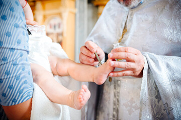 Obraz na płótnie Canvas The sacrament of the baptism of a child in an Orthodox church, the priest anoints the baby's feet with holy oil.