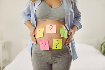 Choosing baby name. Cropped image of pregnant woman with many colored stickers on her abdomen...