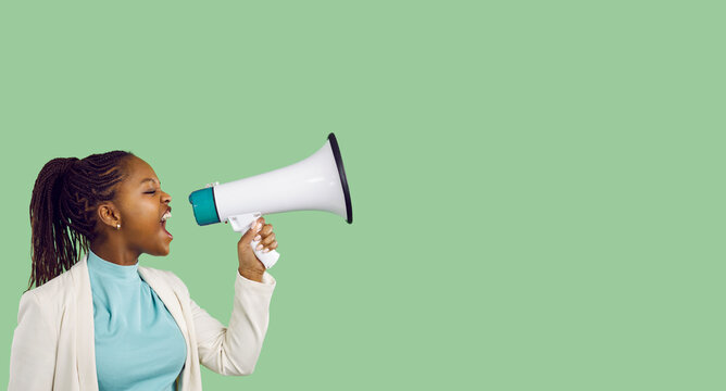 Confident beautiful young black woman holding and yelling through megaphone. Loud activist girl makes important news announcement standing on blank green colour text copyspace studio banner background